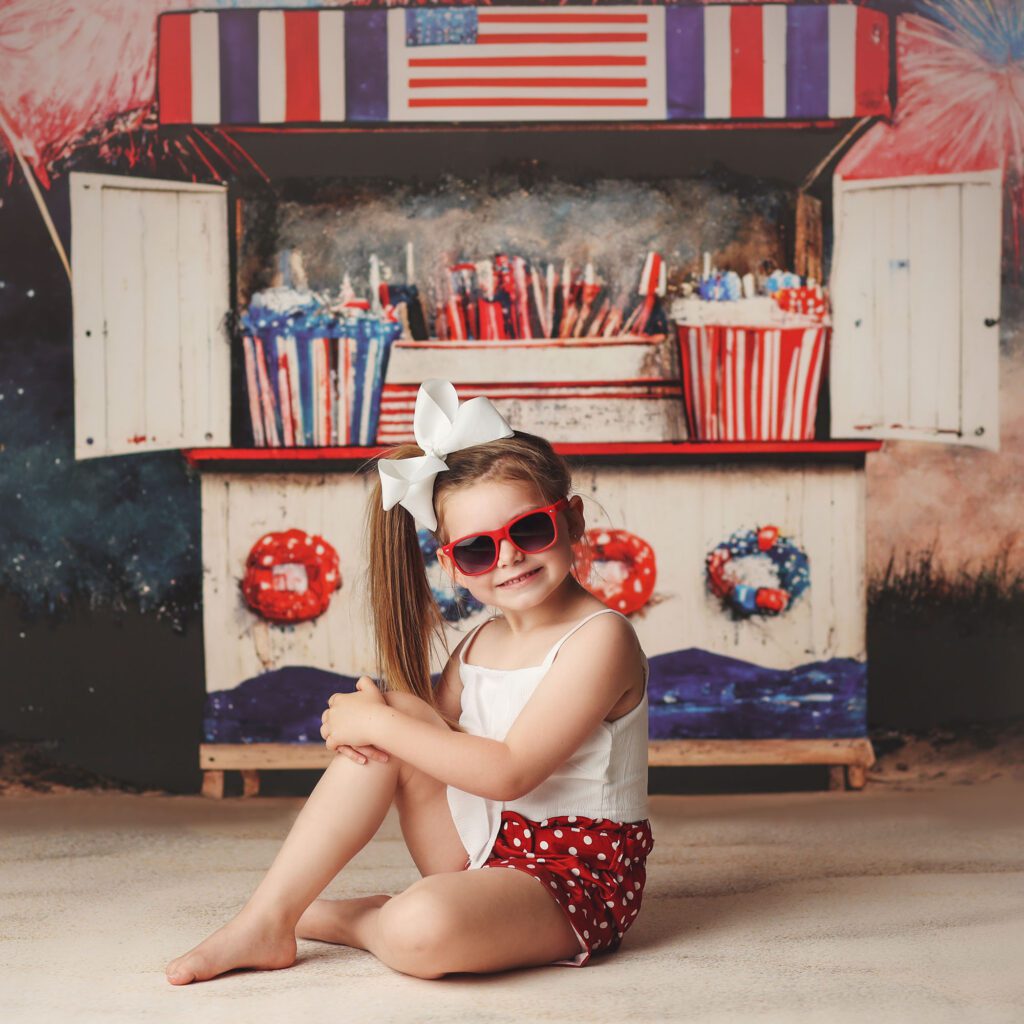 Little girl wearing sunglasses in a Fourth of July beach themed studio portrait