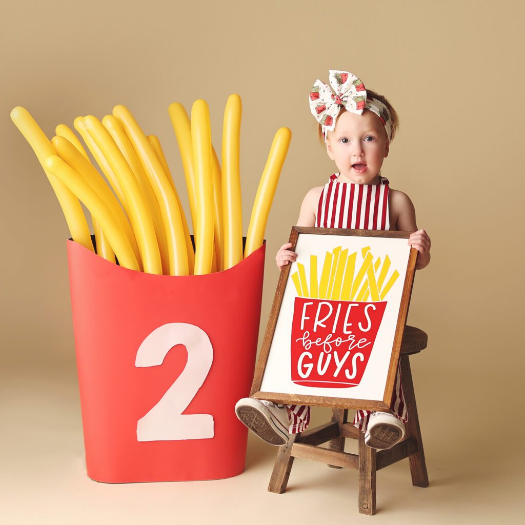 Two year old girl holding a fries before guys sign in a birthday studio portrait