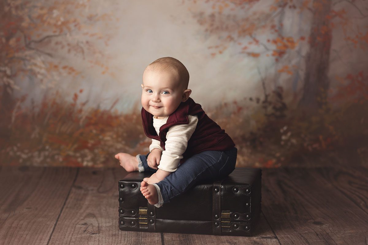Kansas City baby milestone sitter session of baby boy sitting ona suitcase in warm tones