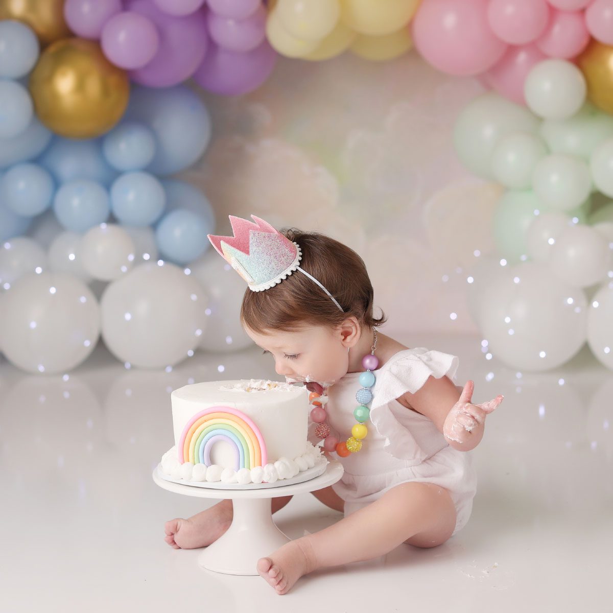 Little girl leaning over to take a bite of her rainbow cake smash cake in Kansas City