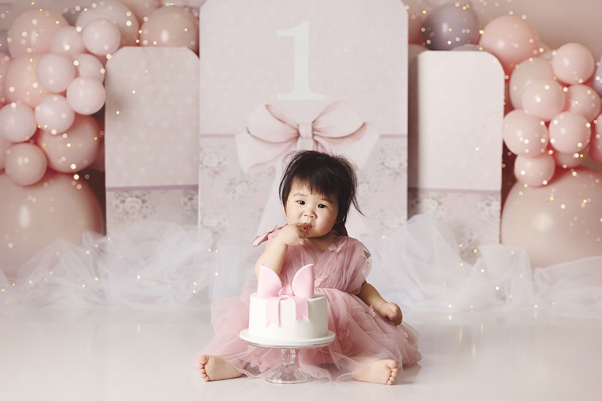 Kansas City cake smash photography studio session with baby girl in pink dress and white cake with a pink bow on top