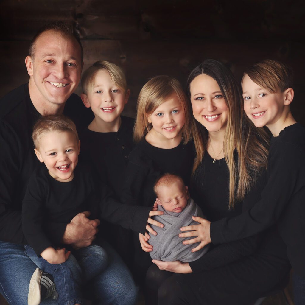 Family of seven holding their newborn baby and smiling at the camera in a studio portrait