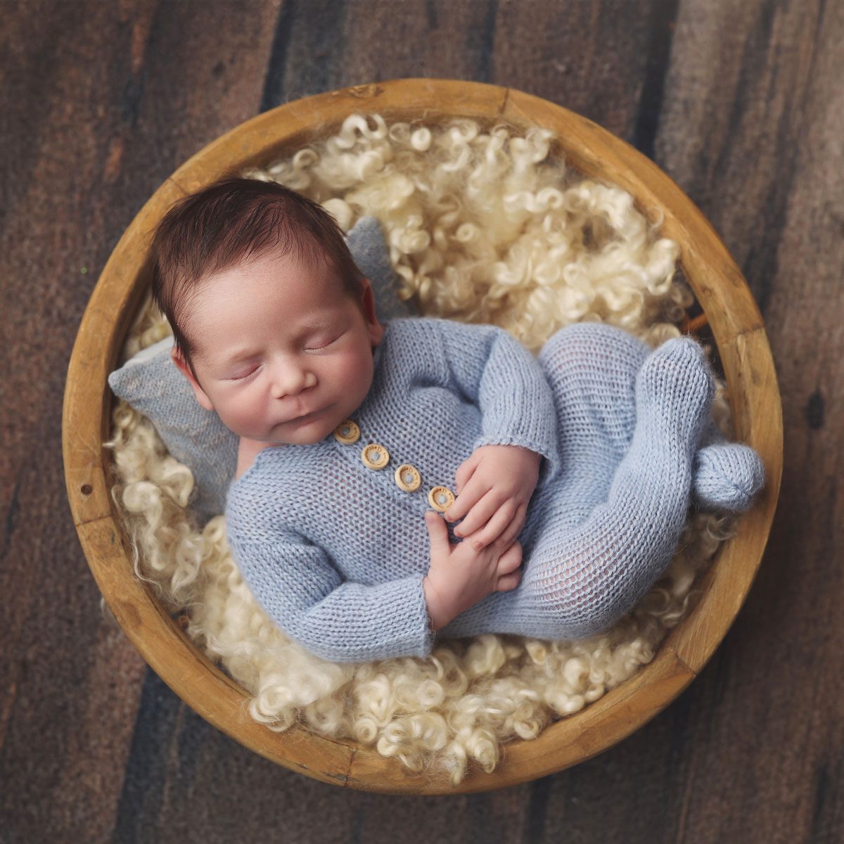 Overhead portrait of a newborn baby boy in a blue knit sleeper lying in a basket during a Kansas City Studio Newborn Session