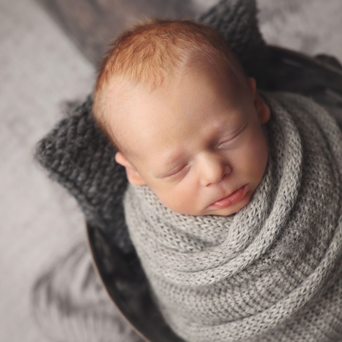 Newborn baby boy wrapped in a gray knit swaddle and photographed in a bucket during a studio newborn session in Kansas City