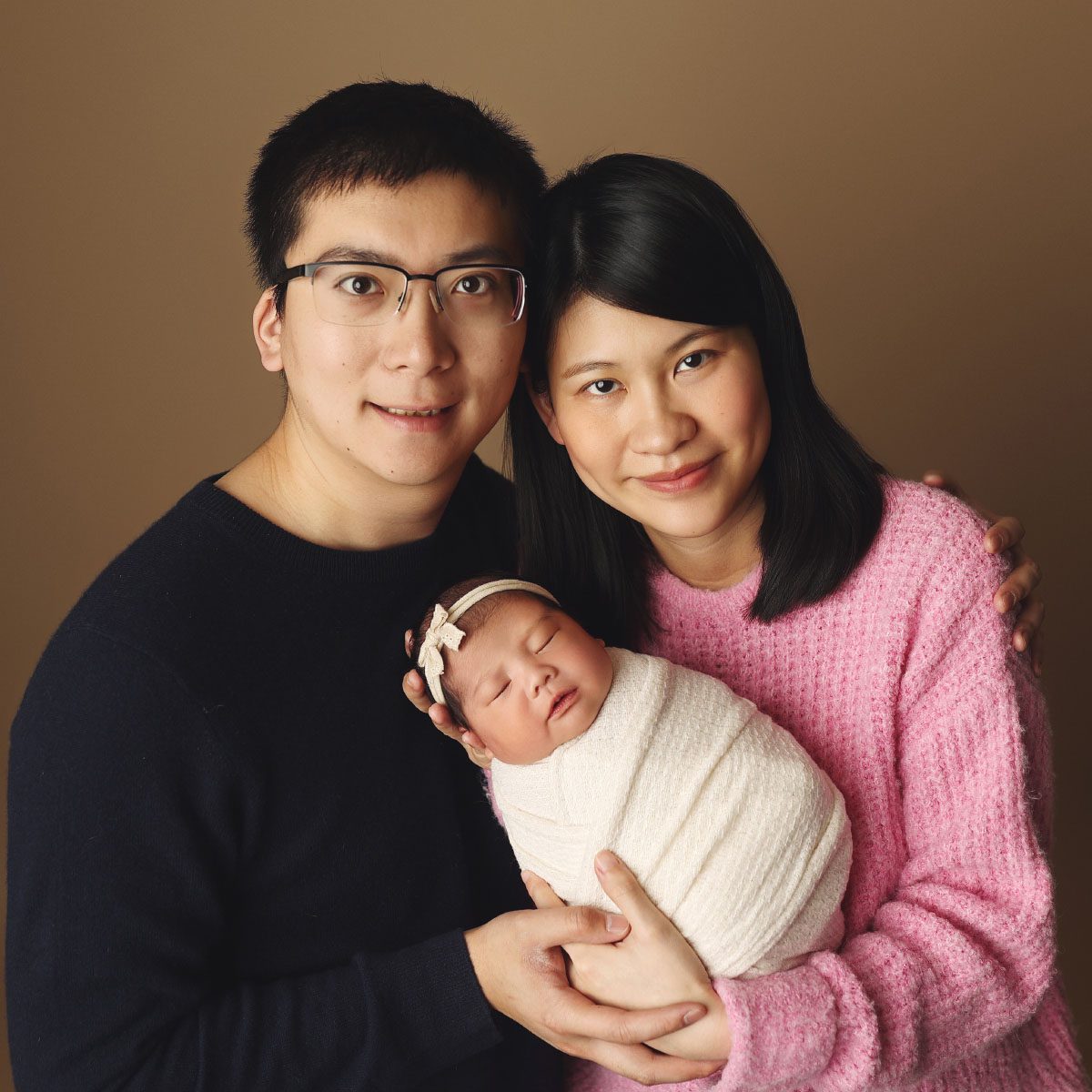 Parents holding their newborn daughter wrapped in white during a studio newborn photography session in Kansas City