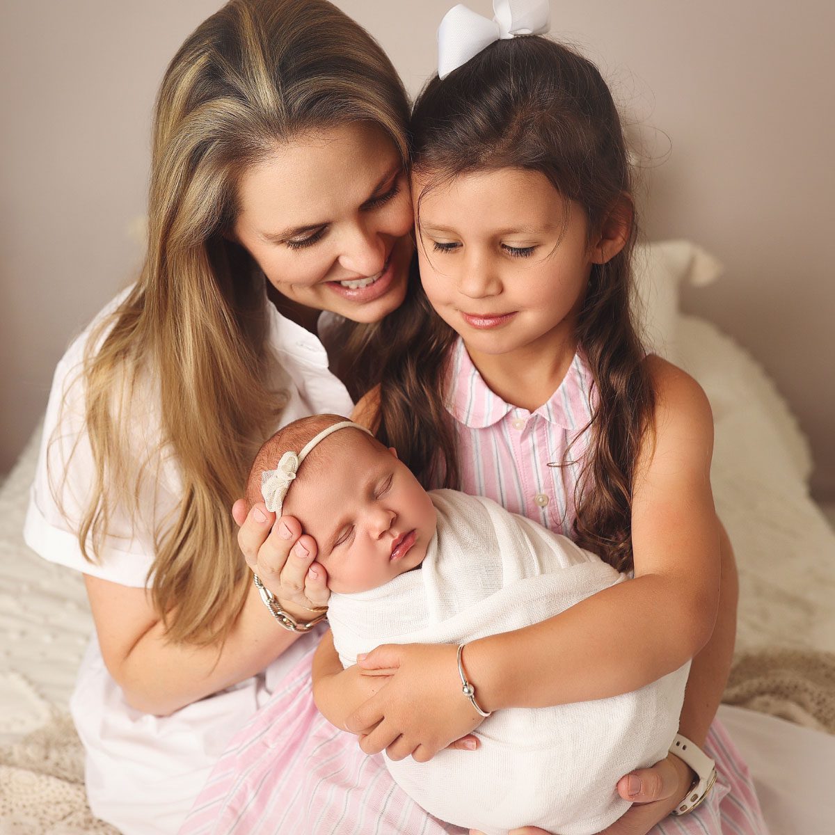 Mother and older sister holding their swaddled newborn baby during a studio newborn photography session in Kansas City