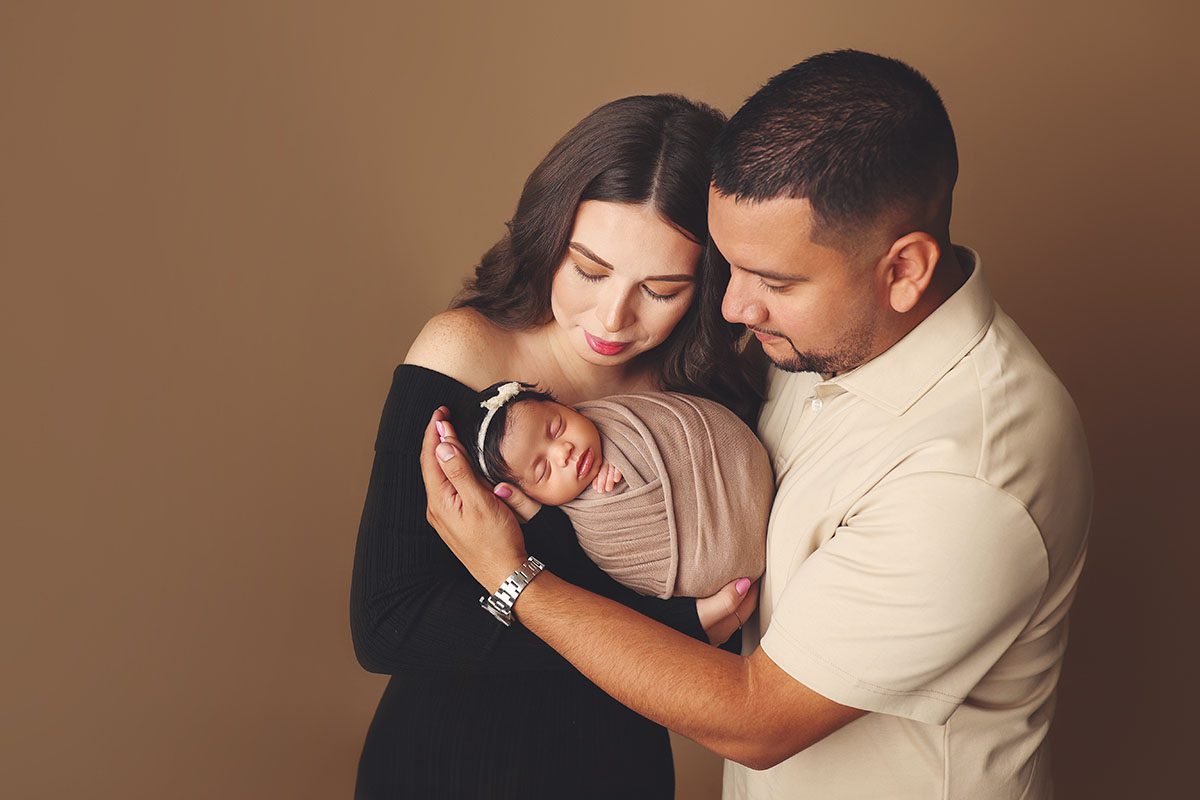 Kansas City newborn photography studio portrait of parents snuggling their wrapped newborn daugther