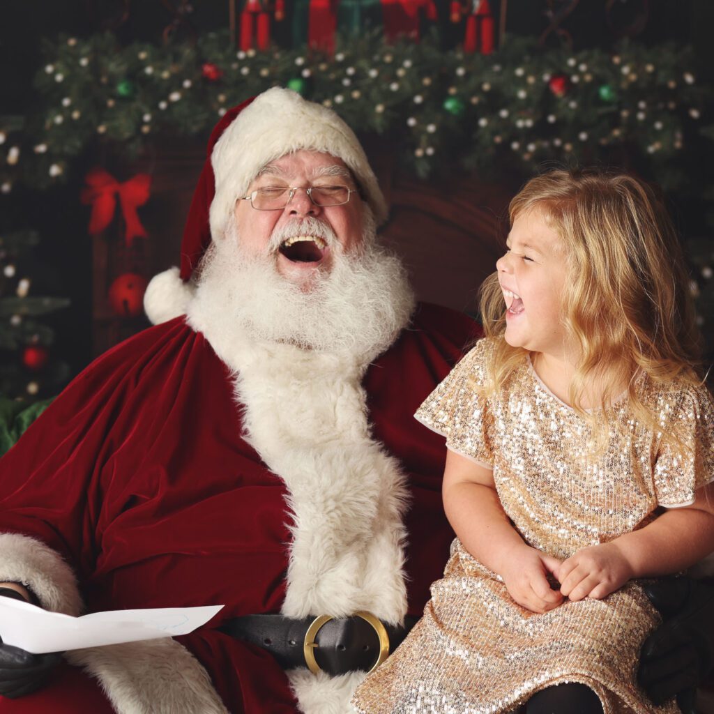 Santa holding a Christmas list while laughing with a little girl in sequin dress