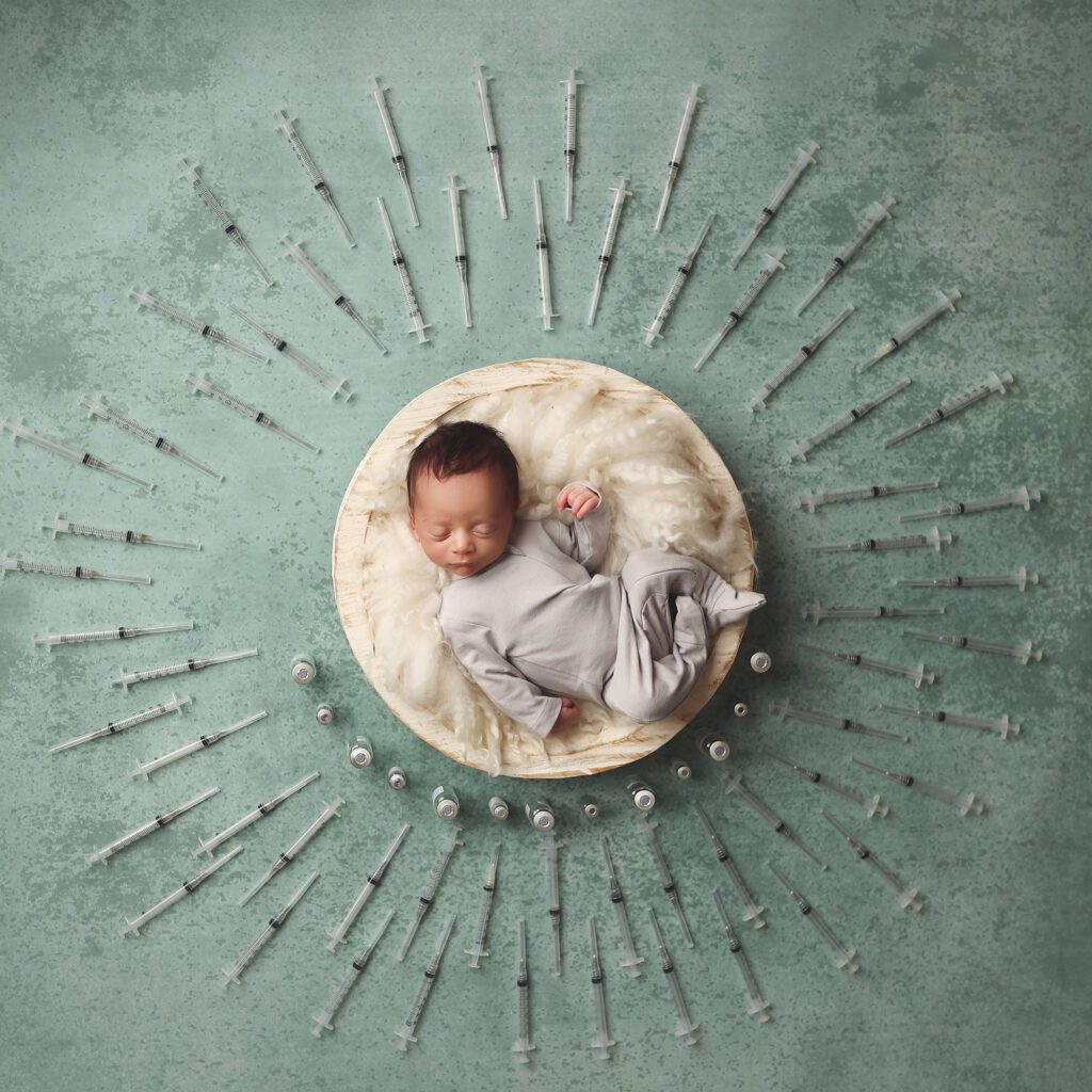 Newborn baby boy in a bowl surrounded by IVF needles arranged in a circular design