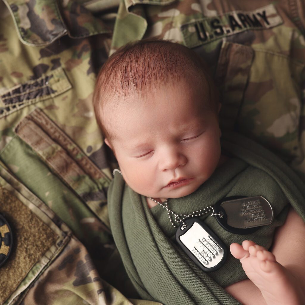 Newborn baby boy wrapped in green laying on his father's army jacket with dog tags around his neck