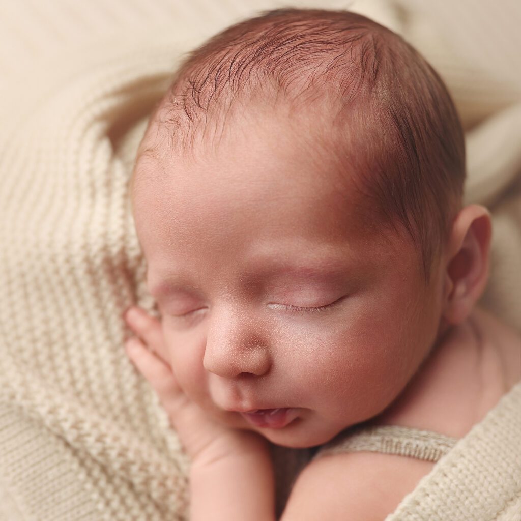 Close-up profile of a sleeping newborn baby on a cream colored blanket