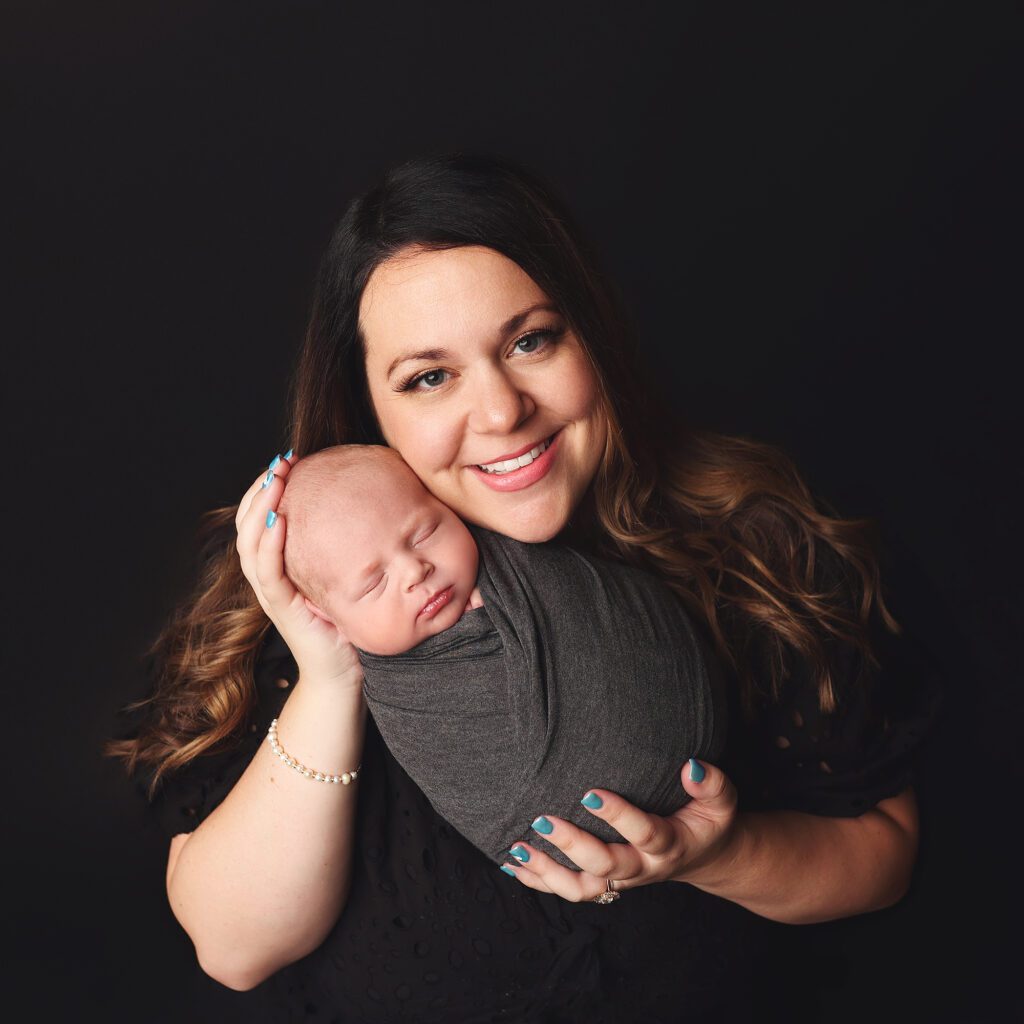 Mother smiling at the camera while holding her swaddled newborn baby boy