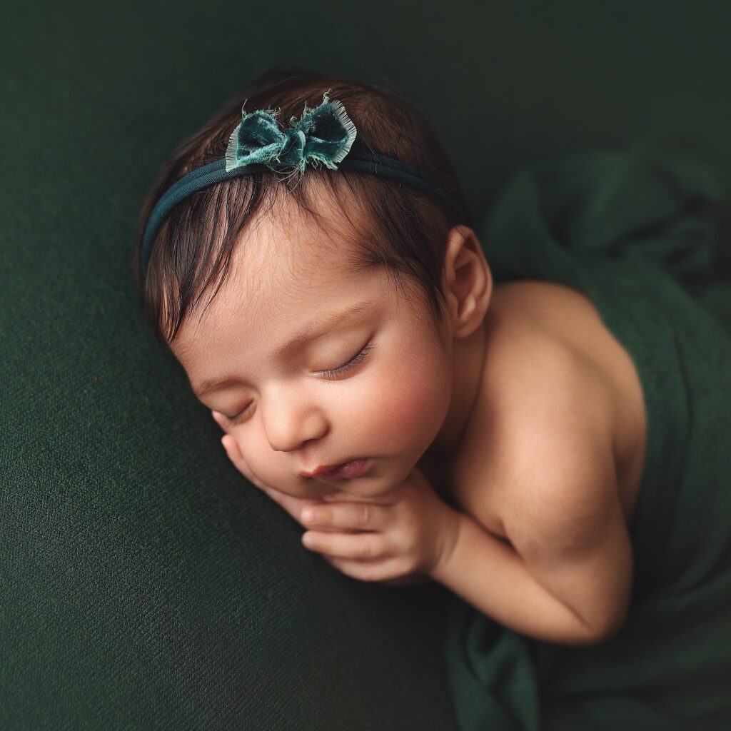 newborn baby girl wrapped in dark green fabric laying on her side in profile