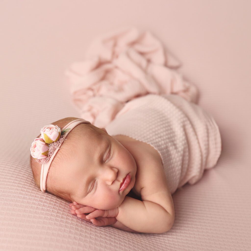 Newborn baby girl wrapped in light pink with hands folded under her cheek
