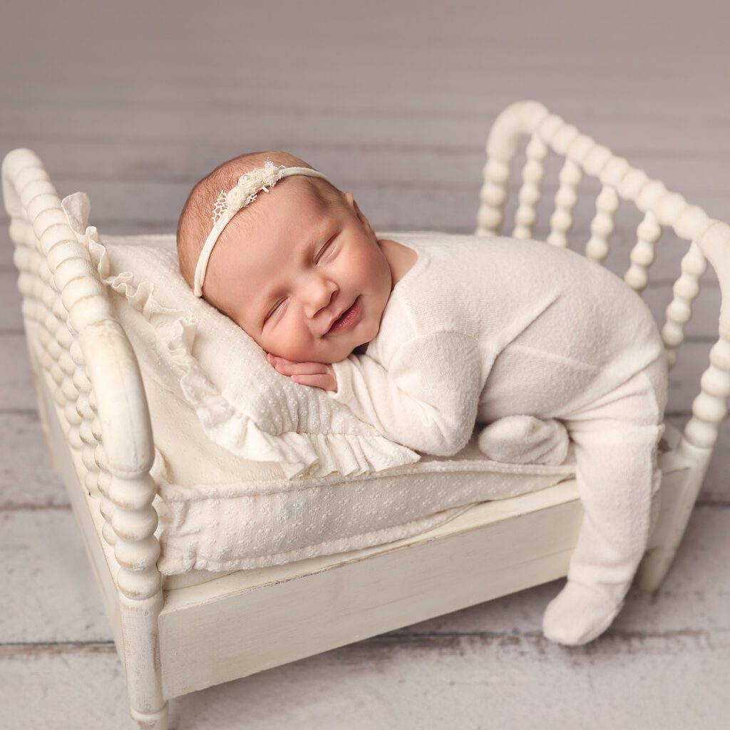sleeping newborn baby girl smiling while lying on a white bed