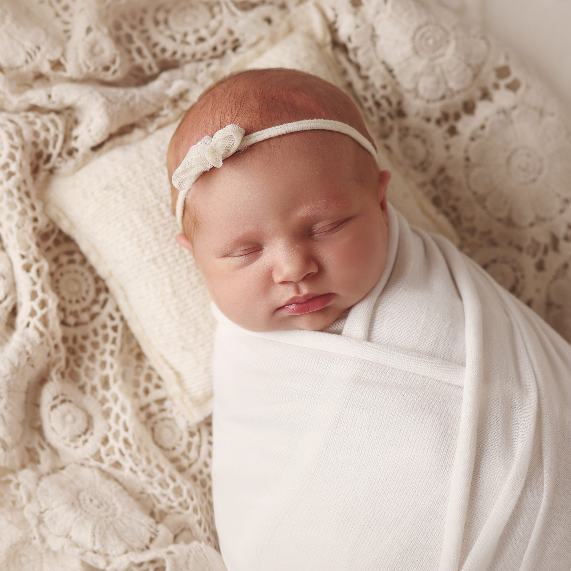 Overhead newborn portrait of a baby girl wrapped in white with bow on head in Olathe Kansas studio