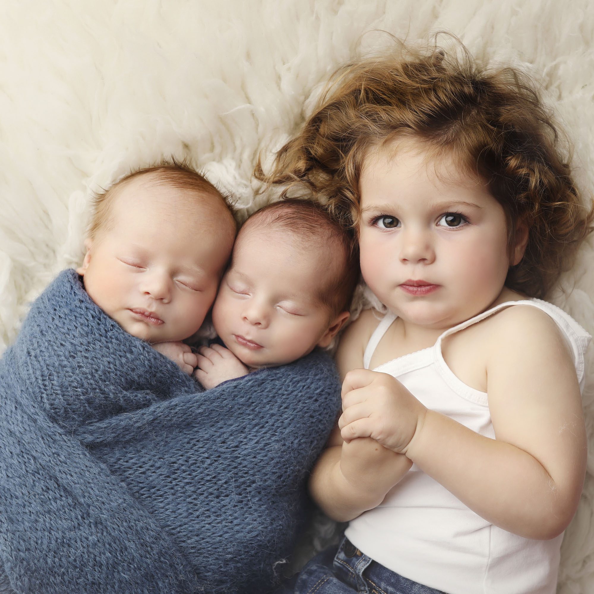 Overland Park, KS sibling newborn portrait toddler girl laying beside twin newborn brothers wrapped in a blue knit