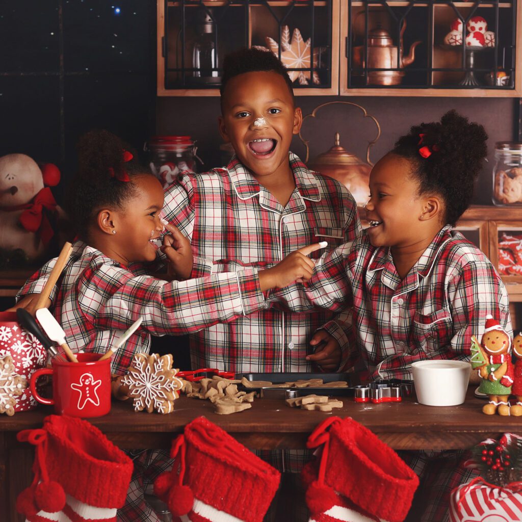 Brother and two sisters laughing and throwing flour in a Christmas kitchen set