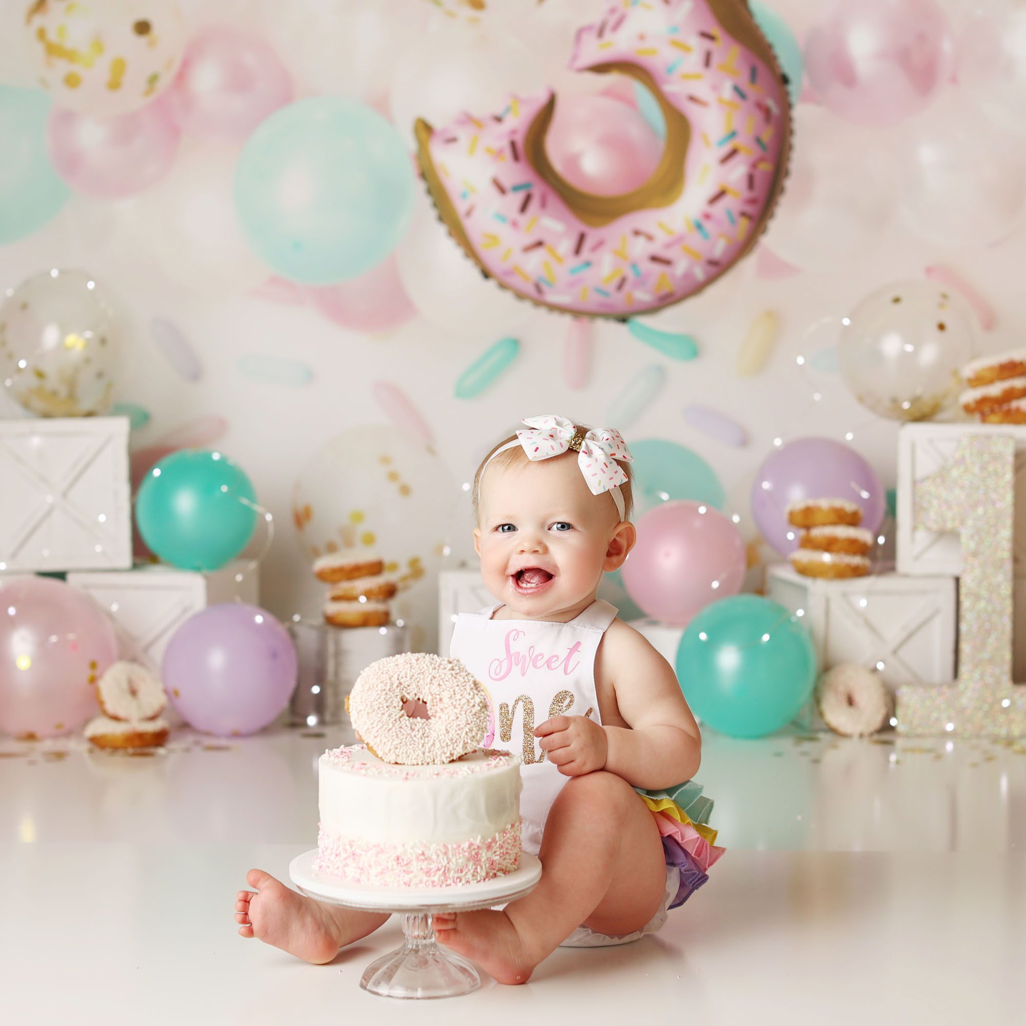 Liberty, MO donut cake smash girl sitting behind cake with donut backdrop and stacked donuts smiling