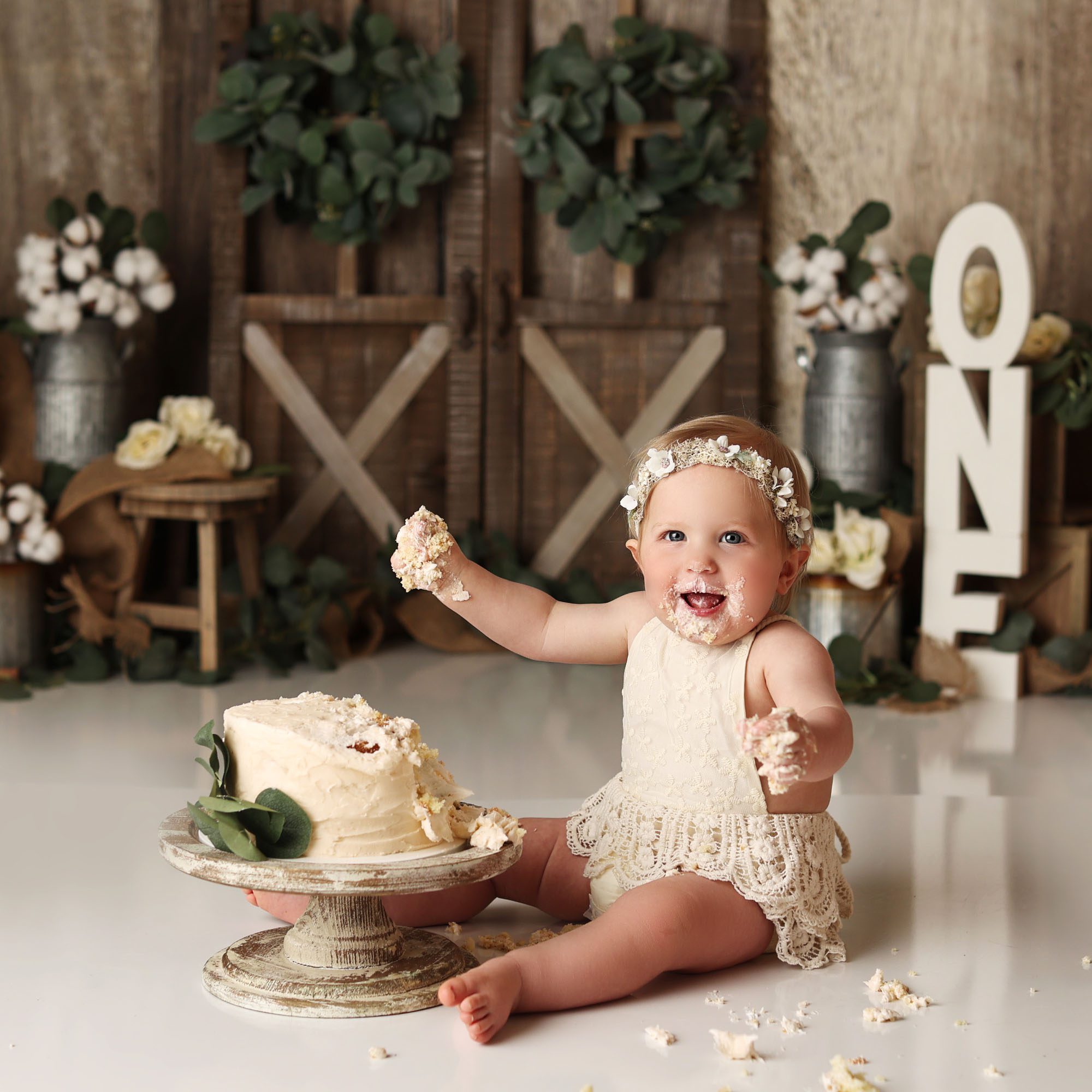 Lee's Summit, MO boho cake smash girl in lace romper and floral crown smiling with cake