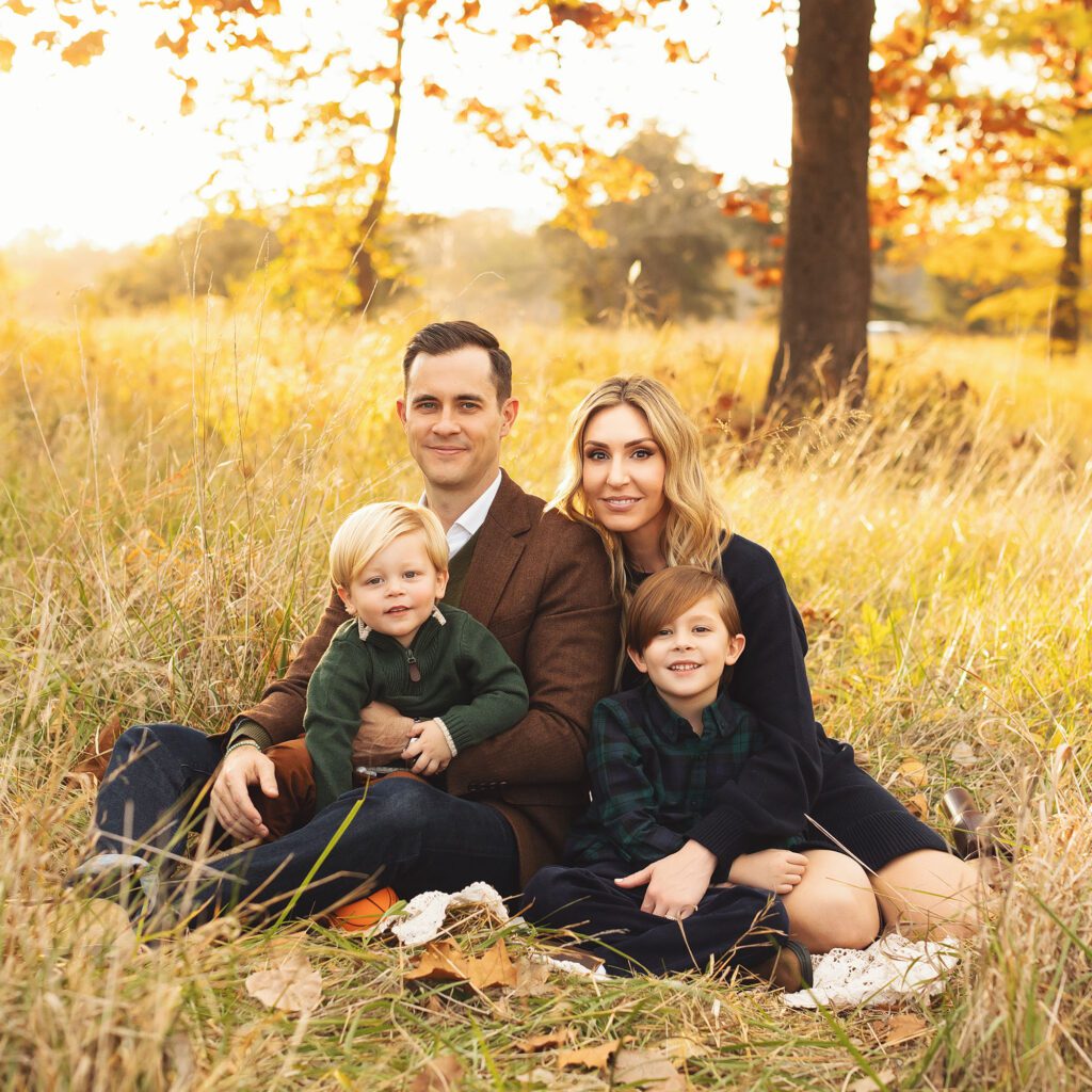 Family with two young sons sitting together in a field during golden hour