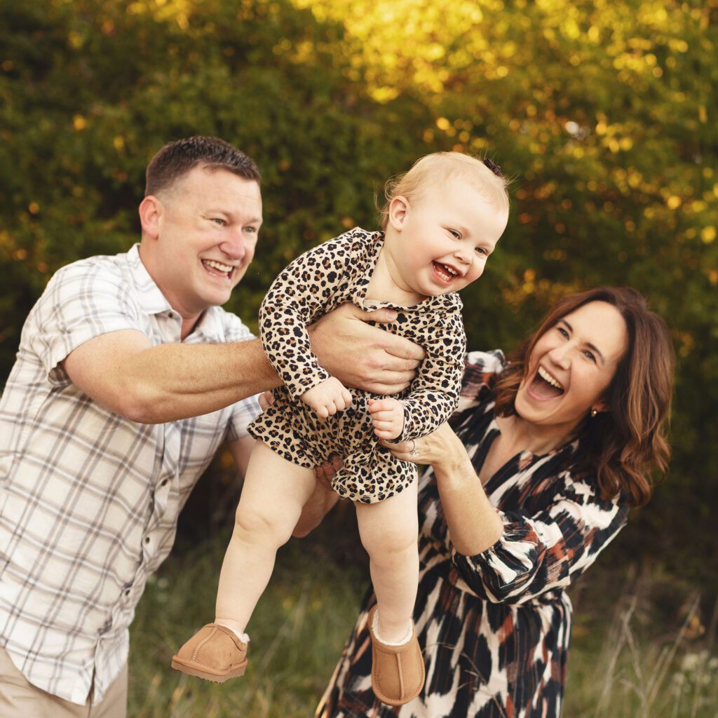 Parents lifting their baby daughter during a playful fall outdoor family session