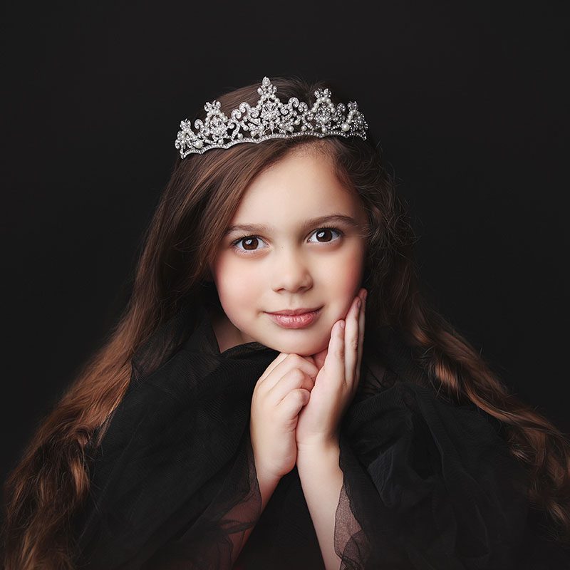 Little girl wearing a princess crown smiling in a studio portrait