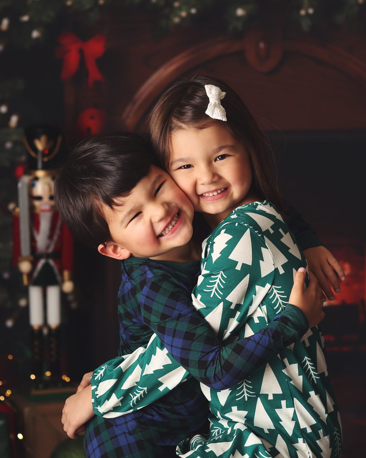 Brother and sister hugging and laughing in front of a Christmas fireplace with a nutcracker
