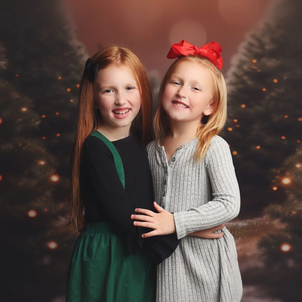 Sisters hugging and laughing in front of a christmas tree farm backdrop