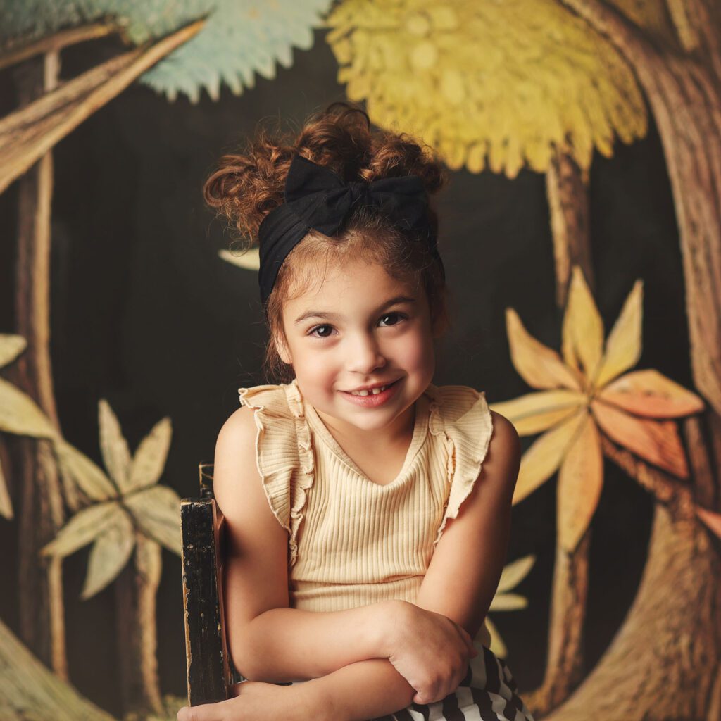 Little girl smiling with a bow in her hair ina storybooked themed studio portrait