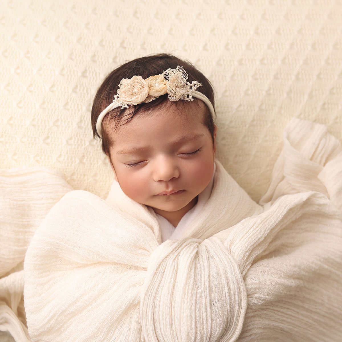 Newborn baby girl wrapped in a cream bow wrap during a studio newborn photography session in Kansas City