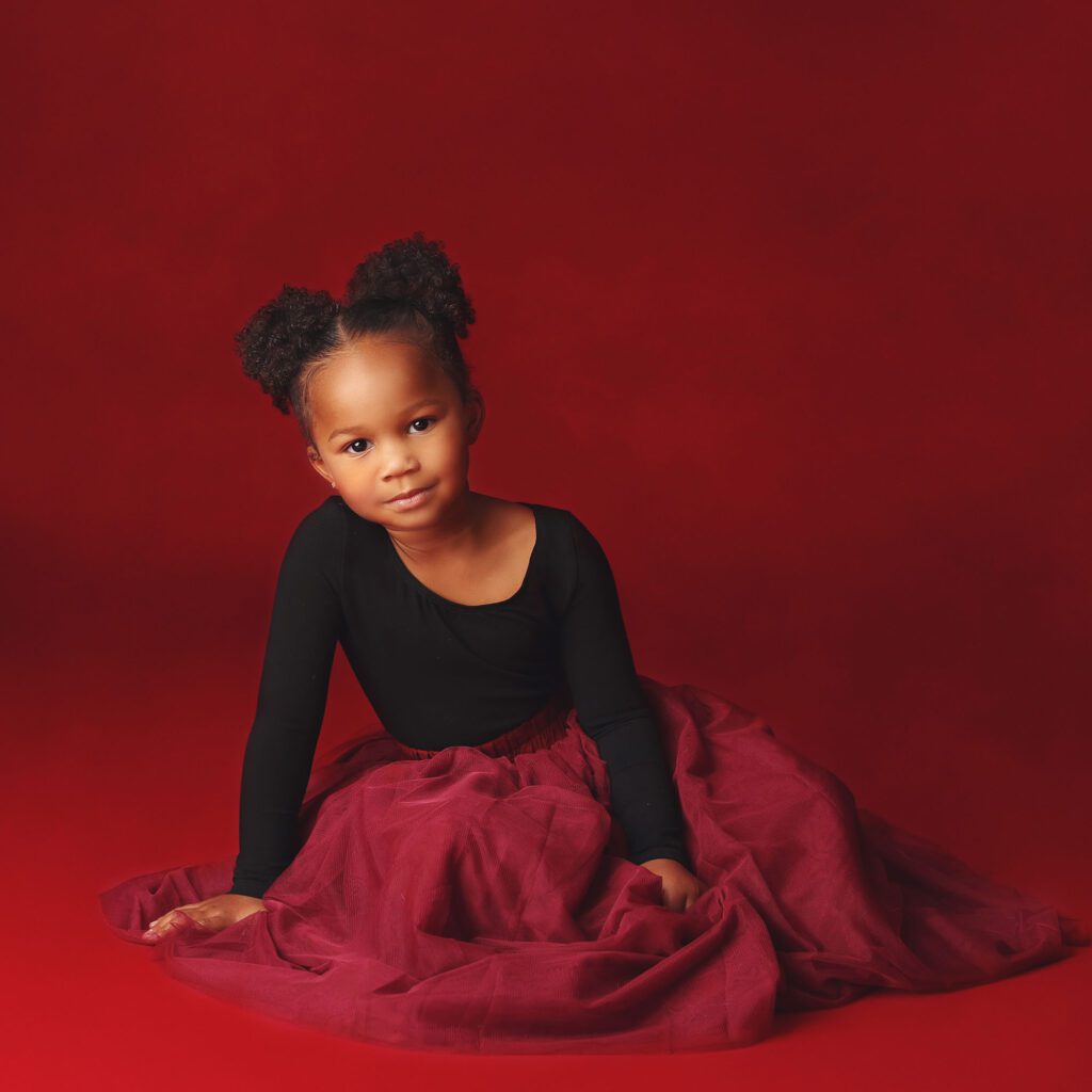 Little girl wearing a red tulle skirt smiling in a studio portrait