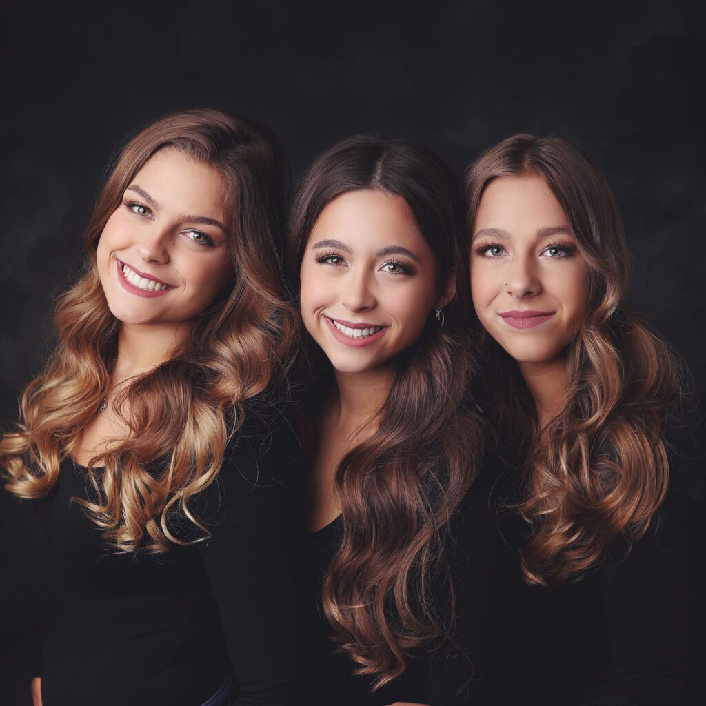 Close up portrait of three teenage sisters smiling against a black backdrop