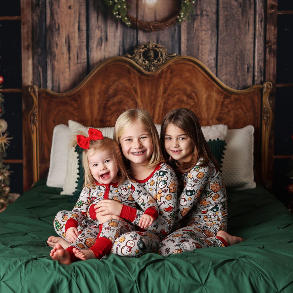 Three sisters wearing Christmas pajamas hugging on a bed