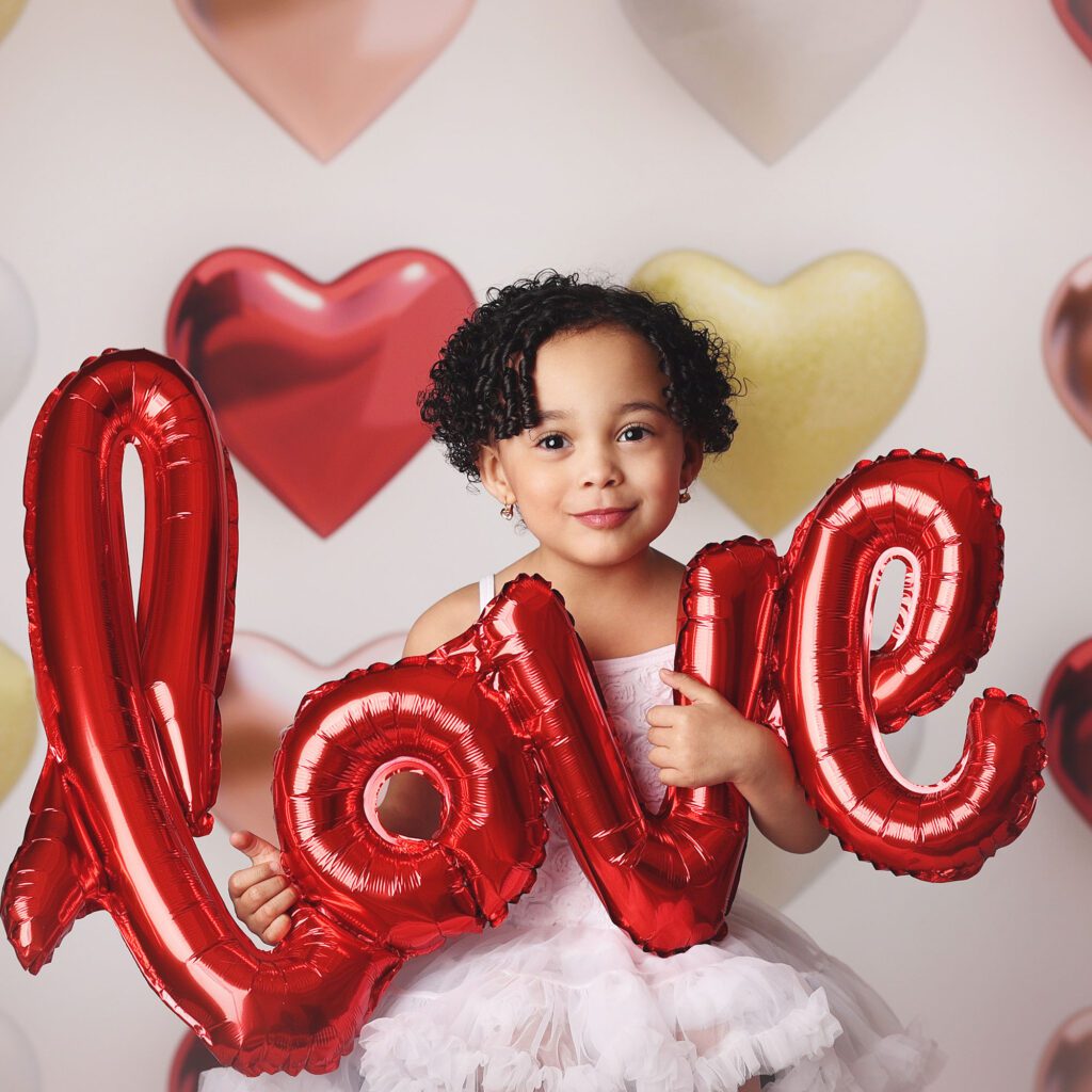 Toddler girl smiing in a studio portrait holding a balloon that spells love