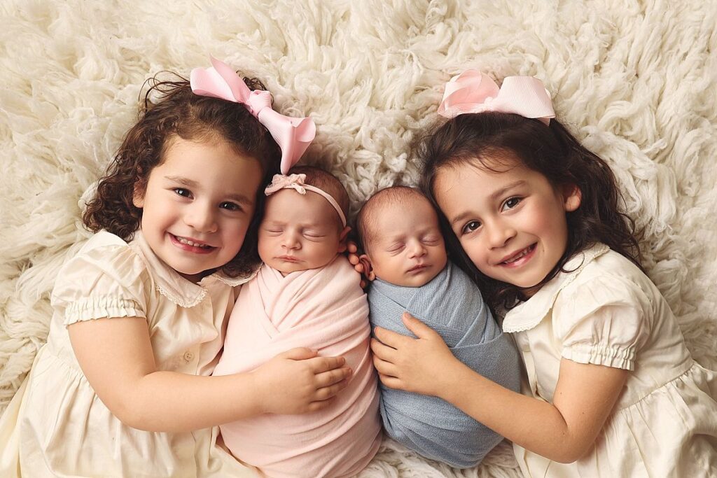 Sibling portrait with two older sisters snuggling newborn twins during a Lee's Summit newborn photography session.